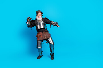 Naklejka premium Elderly man in medieval knight armor posing with a cheerful expression against a vibrant blue backdrop, evoking history