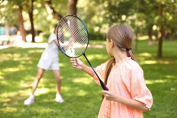 Little girl with badminton racket and shuttlecock playing with her friend in park, selective focus