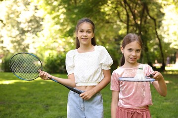 Portrait of smiling little girls with badminton rackets and shuttlecock in park