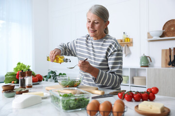 Senior woman cooking salad at white marble table in kitchen