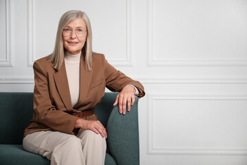 Portrait of beautiful senior woman on sofa near white wall. Space for text