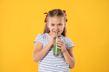 Little girl drinking juice through straw on orange background
