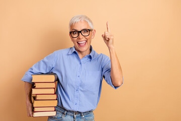 Confident Senior Woman Holding book While Gesturing a Pointing Sign, Wearing a Blue-striped Shirt...