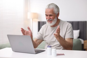 Senior man having online consultation with doctor via laptop at table indoors
