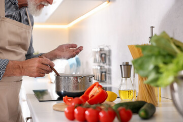 Elderly man cooking dish on cooktop in kitchen, closeup