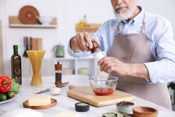 Elderly man cooking at white marble table in kitchen, closeup