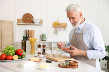 Elderly man cooking at white marble table in kitchen
