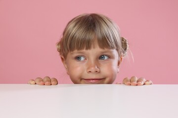 Curious little girl peeking over table against pink background