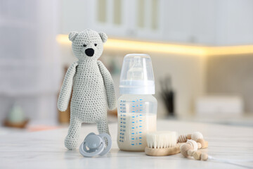 Bottle with milk, toy bear and baby accessories on table indoors