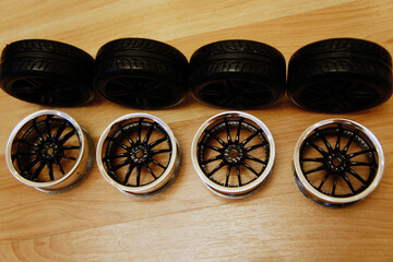 Set of black model car tires and rims arranged on wooden surface