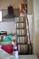 A stack of stainless steel cooking pots in a budget kitchen, with simple household items and utensils creating a modest yet practical cooking space
