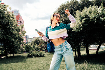 Young woman enjoying music on headphones while dancing happily in an outdoor urban park with bright...