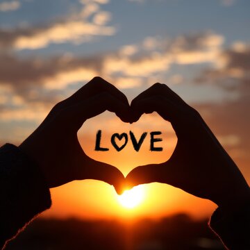 Romantic silhouette of hands forming a heart shape with LOVE written inside against a sunset sky. A beautiful expression of love and affection.