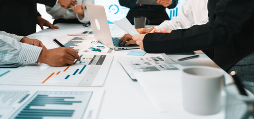 A diverse group of professionals collaborates in a modern office setting, analyzing charts and data on a laptop during a business meeting focused on strategy development. SACTR