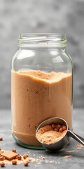 Smooth creamy peanut butter filling a glass jar with a spoon full of nuts and peanut butter
