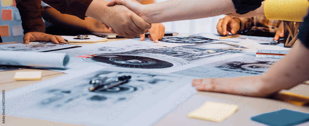 Poster a close-up view of hands shaking in agreement over design sketches on a table. the scene depicts tea