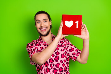 Excited young man showcasing a vibrant red box with a heart icon on a bright green background,...