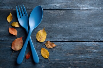 A blue spoon and fork crossed on a blue wood surface surrounded by autumn leaves
