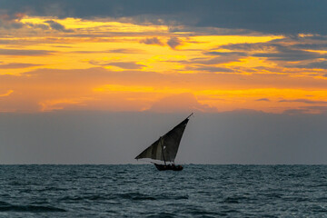 A traditional Swahili Dhow sailing off the coast of Zanzibar in the Indian Ocean during sunrise.