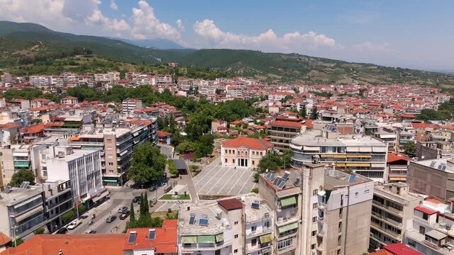 Aerial Drone View of Veria City's Central Clock Tower Square and Surrounding Mountains in Northern Greece on a Bright Summer Afternoon.