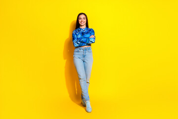 Casually dressed young woman posing against a bright yellow background, embracing modern style and...