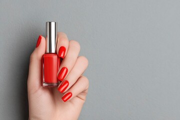A hand holding a bottle of red nail polish against a gray backdrop