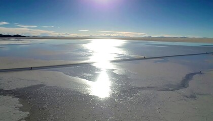 Sun glares on reflective salt flat under a blue sky, with distant hills visible