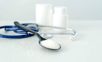 A spoon with salt on it is on a table next to a stethoscope and two pill bottles
