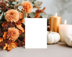Blank vertical card mockup on the table styled with orange dahlias, golden candles, and white pumpkins