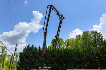 Concrete pump truck stands tall against bright blue sky while workers prepare construction site in...