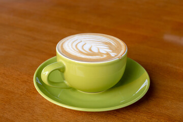 A side-angle close-up of a classic latte in a vibrant green ceramic cup, showcasing a perfect rosette design in the milk foam on a rustic wooden table.