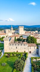 High-angle view of a historic town with stone buildings, gardens, and a fortress-like structure, bathed in natural light.
