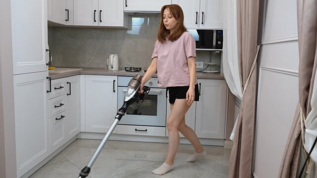 Cheerful homemaker grooving with cordless vacuum, transforming routine kitchen cleaning into playful, energetic dance performance within bright, modern apartment interior
