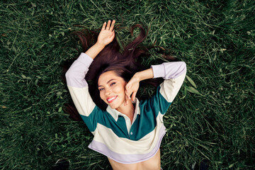 Positive happy woman lying in grass wearing a casual sweatshirt, enjoying leisure outdoors during a...
