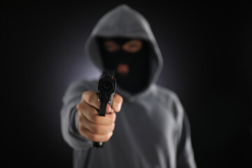 Criminal in mask with gun on dark background, selective focus