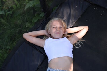 Cute little girl lying on black trampoline outdoors, top view
