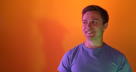 Smiling man in neon lights against orange background. Space for text