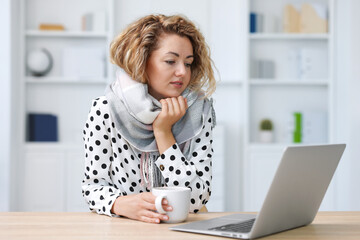 Air conditioning. Woman with scarf and cup of hot drink suffering from cold temperature at...