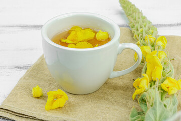 Cup of herbal tea with mullein flowers and leaves on neutral wooden background. Natural light