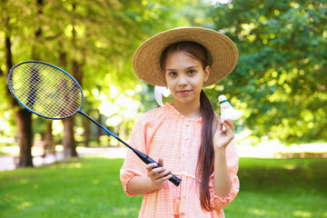 Portrait of cute little girl in hat with badminton racket and shuttlecock in park