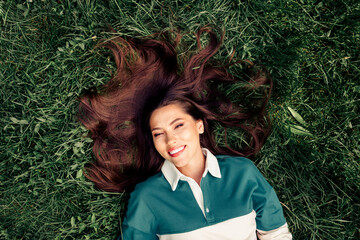 Young woman lying on grass with a bright smile, showcasing natural beauty and a trendy style in an...