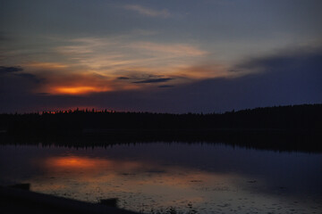 A breathtaking sunset reflecting on a calm lake, surrounded by forested scenery, creating a peaceful and serene atmosphere perfect for relaxation.