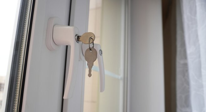 Close-Up of Locked White PVC Window Handle with Two Inserted Keys in Bright Interior with Sheer Curtain, Representing Home Safety, Modern Security, and Window Lock Mechanism Concept
