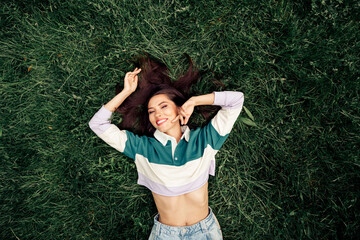 Positive woman relaxing outdoors on grass enjoying a sunny day with a cheerful smile and casual trendy clothing style.