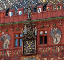The facade of the 'red house' - the town hall in Basel, with a clock, a statue of a knight with the city's coat of arms and interesting paintings