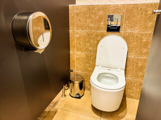 Public restroom interior with toilet and metal bin near tiled wall. Sanitation, hygiene, and facility design for cleanliness, comfort, and guest convenience.