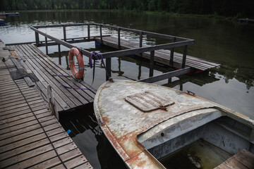 A weathered boat rests near a rustic wooden dock, surrounded by calm waters and lush greenery, capturing a serene yet neglected lakeside scene.
