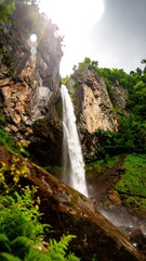 Waterfall cascading down rocky cliffside, lush greenery
