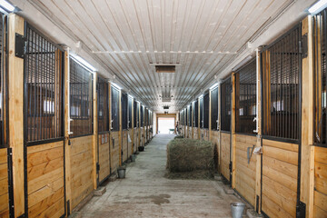 A well-lit horse stable featuring wooden stalls, completed with spacious interiors and hay bales, ideal for equine care and boarding.