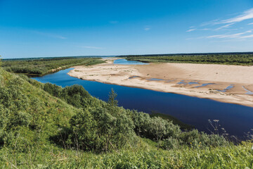 A tranquil river flows through a verdant landscape under a clear blue sky. Perfect for nature lovers and outdoor enthusiasts seeking peace and beauty.